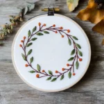 a handmade floral wreath embroidery featuring green leaves and orange berries