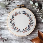 a handmade floral wreath embroidery featuring terracotta and bright blue leaves