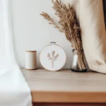 a simple wildflower embroidery piece displayed on a table with decorative items