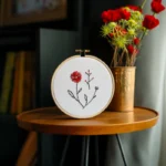 a small table with a hand embroidery artwork and a bouquet of roses beside it