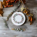 a wreath embroidery displayed with leaf decorations beside it