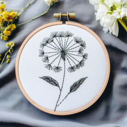 black and white dandelion line embroidery displayed on a blue-gray fabric