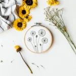 dandelion embroidery with seven flowers, displayed in a hoop with decorative blossoms beside it