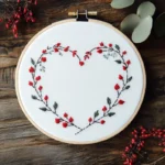 heart-shaped wreath embroidery featuring green leaves and red flower centers
