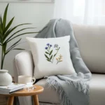 light gray sofa with a light blue throw blanket and a white embroidered cushion