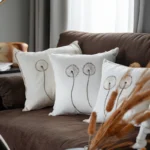 sofa decorated with three white fabric cushions featuring dandelion embroidery patterns