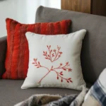 two pillows on the sofa, one in red and one in white with red floral embroidery