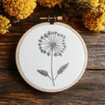 white dandelion hand embroidery placed on a dark brown wooden table