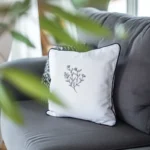 white pillow on a gray sofa, embroidered with a black line-art wildflower design