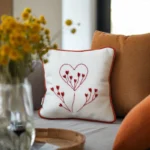 cushions arranged on a sofa, with small daisies displayed in a vase nearby