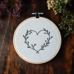 hand embroidery displayed on a table, featuring a heart design accented with leaves