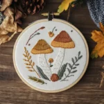 brown embroidered mushrooms in a wooden hoop with autumn leaves
