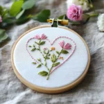 close-up of a delicate pink floral heart embroidery design inside a wooden hoop