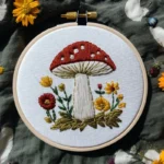 close-up of a hand-stitched red toadstool and flower needlework pattern in a wooden hoop