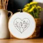 close up of a minimalist botanical heart embroidery design inside a wooden hoop with yellow flowers
