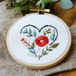 close-up of a simple red floral heart embroidery pattern with green leaves in a wooden hoop