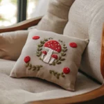 decorative cushion featuring a stitched fly agaric and botanical wreath design