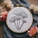 hand-stitched black line mushroom needlework displayed on draped cloth with floral accents