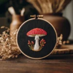 hand-stitched fly agaric mushroom embroidery in a hoop on black fabric