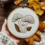hand-stitched mushroom and autumn leaf embroidery in a wooden hoop