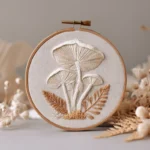 hand-stitched textured mushroom and fern motif in a wooden embroidery hoop