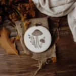 mushroom embroidery hoop displayed with white linen fabric and dried flowers