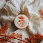 orange mushroom hand embroidery pattern in a wooden hoop with ferns
