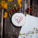 red floral heart needlework in a hoop on a dark wooden table