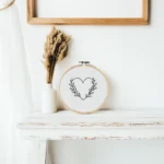 simple black leafy heart needlework in a hoop on a distressed white table next to dried grass