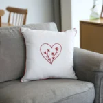 small white cushion with a red stitched flower heart on a grey sofa