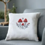 stitched red mushroom and botanical motif on a white decorative cushion