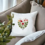 two white throw pillows featuring identical red stitched floral heart designs resting on a grey sofa