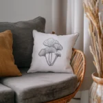 white cushion with simple black stitched mushrooms resting on a chair next to a textured mustard pillow