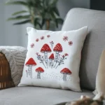 white throw pillow featuring a red woodland mushroom and floral embroidery pattern