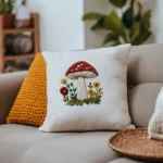 white throw pillow featuring a stitched red mushroom and flowers resting on a beige sofa