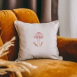 white throw pillow with a pink line art mushroom embroidery on a yellow armchair